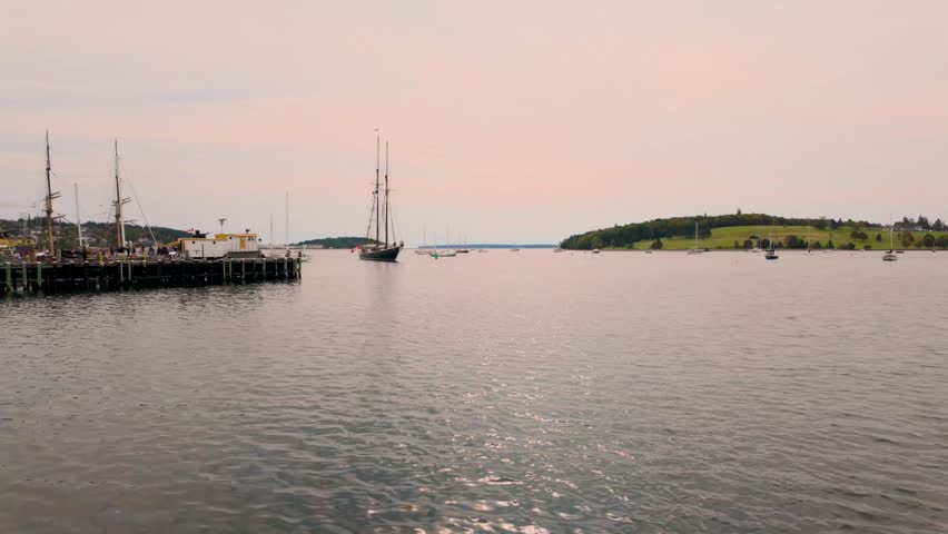 Slow motion footage overlooking the harbour at Lunenburg in Nova Scotia Canada featuring traditional sailing vessels calm coastal waters and a peaceful maritime scene beneath a lightly clouded evening sky