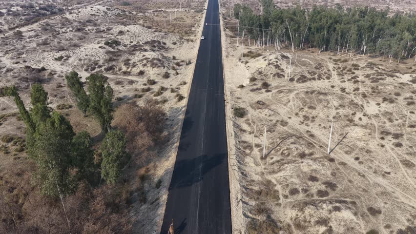 Aerial drone view of a A long straight road stretches through a barren landscape with sparse vegetation on either side and distant trees 4k footage 