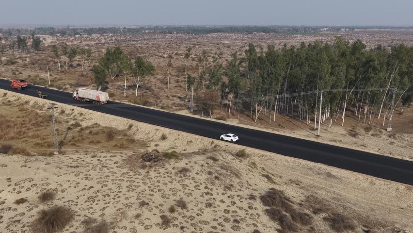 Aerial vie of a Newly paved road surrounded by sparse vegetation and a line of trees on one side with a distant landscape beyond