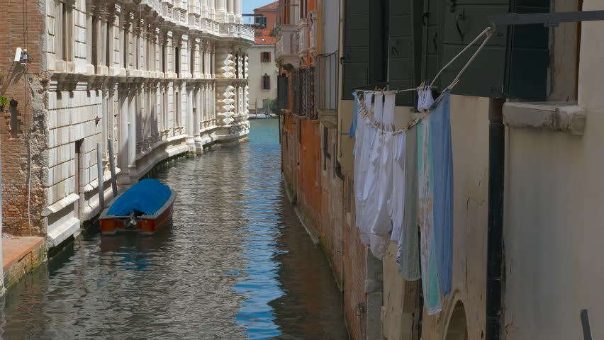 Clothes hanging over a venetian canal. Colorful laundry hanging above narrow venetian canal, with traditional wooden boat moored below, capturing authentic daily rhythm of venetian urban life
