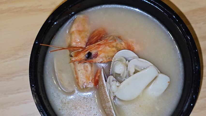 assorted seafood creamy soup of shrimps, squid, crabs, fish fillet, herbs, dill, garlic and onion, seafood mixture hot soup, healthy food concept of pieces of various sea food, selective focus