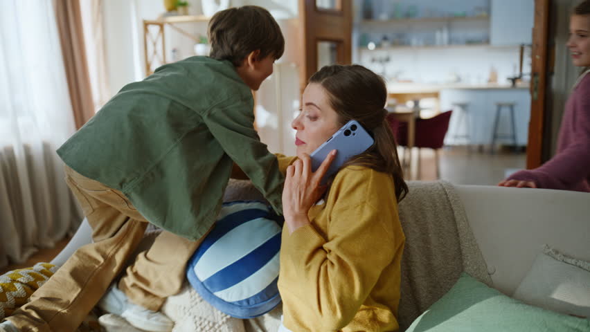 Mother businesswoman working home calming down hyperactive kids closeup. Freelancer woman calling mobile phone active children shouting playing loudly. Noisy son daughter disturbing mom running around