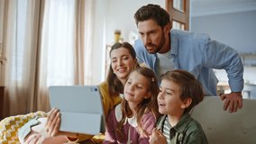 Cheerful family video calling by tablet gesturing to web camera in modern apartment closeup. Surprised kids talking to pad computer webcam enjoying online meeting sitting with parents at home sofa - Powered by Shutterstock - Get 15% off with code: PIKWIZARD15