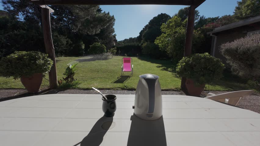 Mate tea ceremony set on a table in a sunny garden with sprinklers watering the green grass. 4K