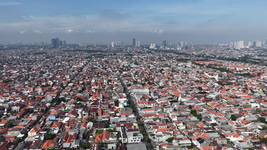 Aerial shot of Surabaya showing dense urban housing, red-tiled rooftops, and a large circular highway interchange surrounded by green space. Captures city life, transportation, and suburban patterns.