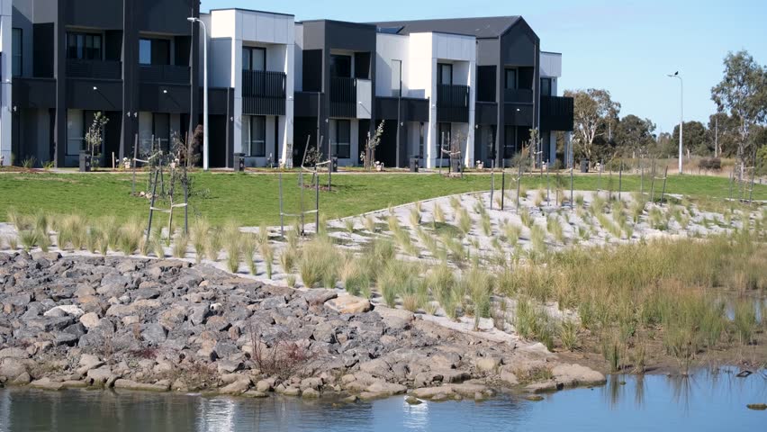 Townhouses overlooking a landscaped drainage basin in a newly developed Australian suburb. Contemporary residential architecture, sustainable urban planning, stormwater management infrastructure