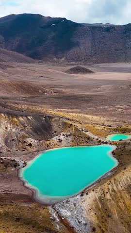Tongariro alpine crossing volcanic landscape with turquoise crater lakes, rugged terrain, vertical drone view, New Zealand.