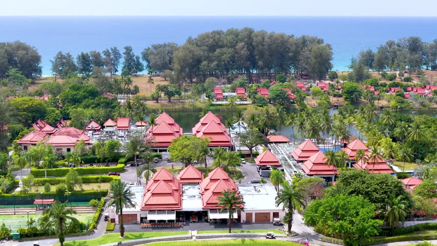 High angle drone shot pans across a tropical luxury resort with red roofs and lakes