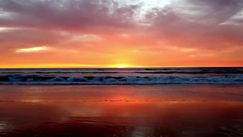 Spectacular ocean beach sunset with fiery orange and red clouds reflected on the water, perfect for nature, travel, and scenic beach visuals.