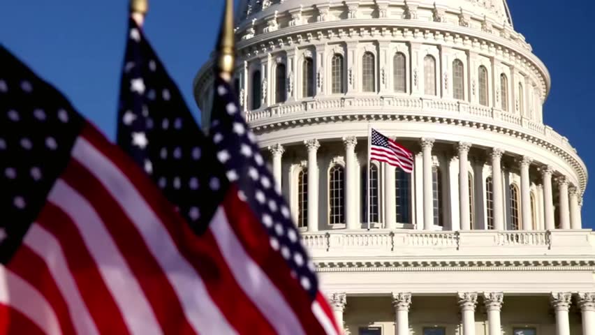 Iconic US Capitol Building with American flags waving in the foreground, ideal for politics, government, history, and national themes.