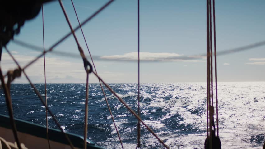 Sailing ropes in foreground with sparkling ocean in background, sunlit waves and open sea horizon, nautical atmosphere and maritime adventure concept.
