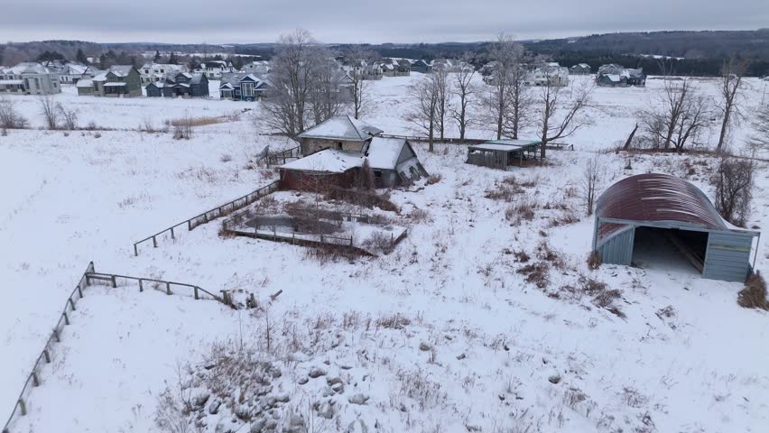 Aerial drone view of abandoned house in winter landscape, covered with snow, surrounded by empty fields, leafless trees, rural area and quiet countryside atmosphere