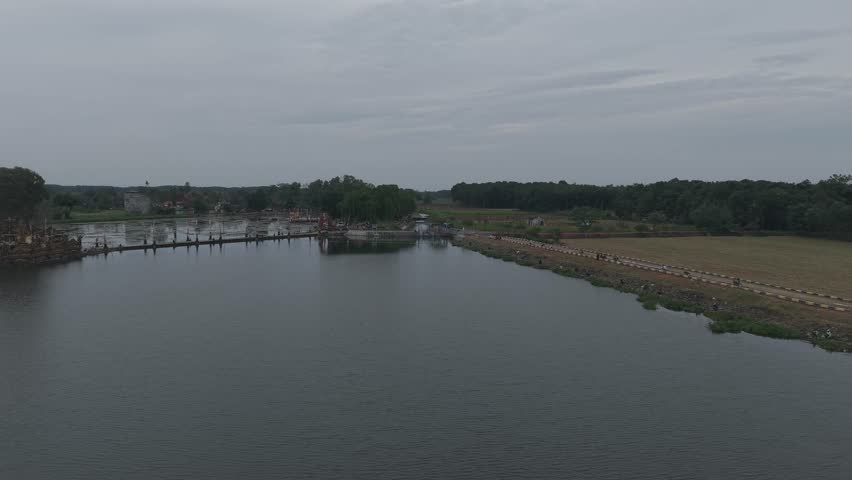 A serene landscape of a body of water surrounded by trees and a field under a cloudy sky