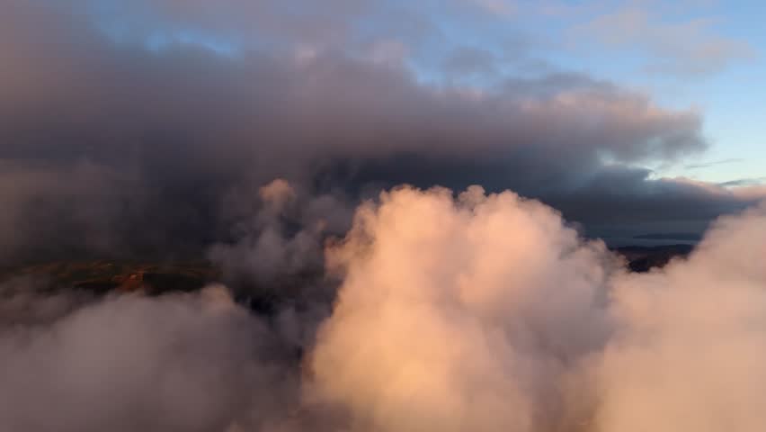 Aerial side pan shot of soft clouds at sunset or sunrise with golden light.