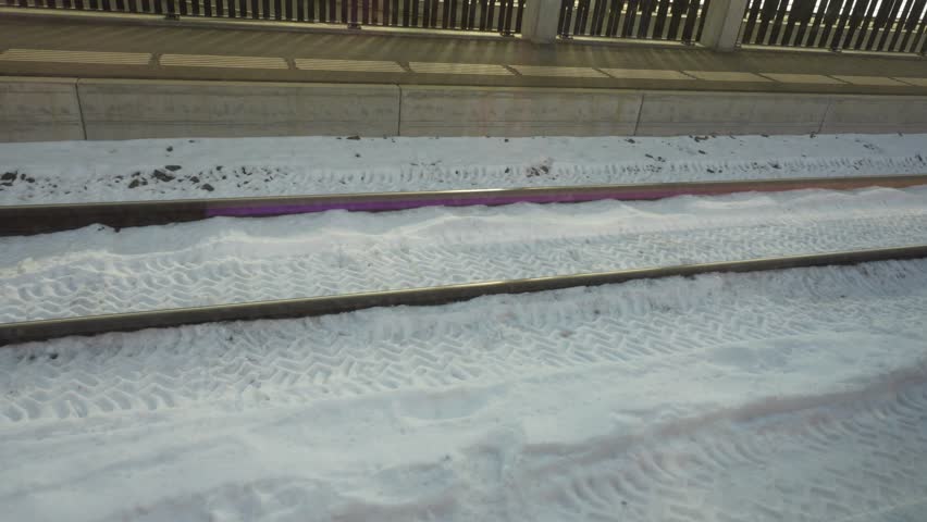 View from a moving train window looking down at snowy tracks and platform on a sunny winter day