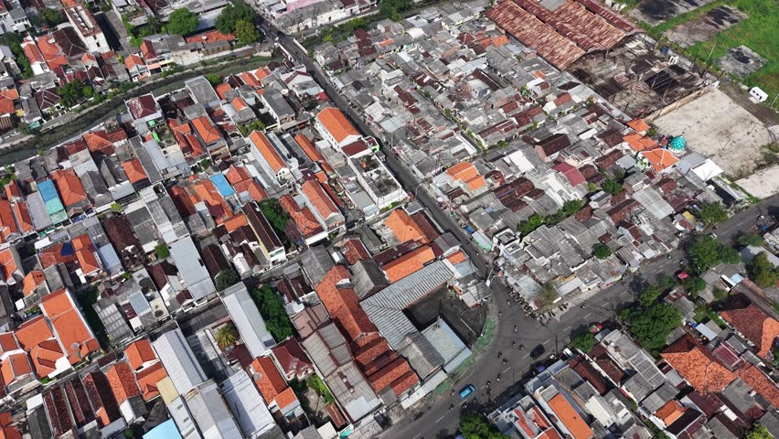 An aerial view of a dense urban neighborhood in Surabaya, showing narrow streets, mixed-use buildings, and vibrant red rooftops that convey lively city life and urban density.