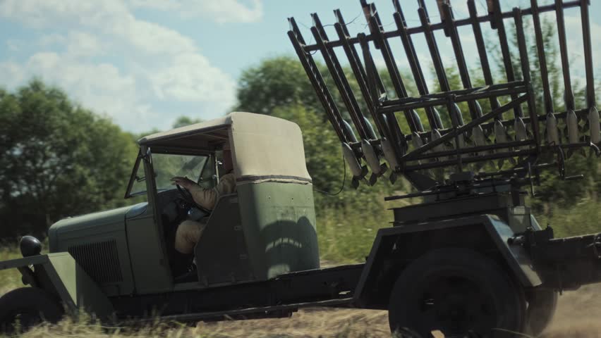 Military vehicle, Soviet Katyusha multiple rocket launcher BM-13, moving along dusty rural road. Sunny day during historical reenactment of Great Patriotic War with onlookers.