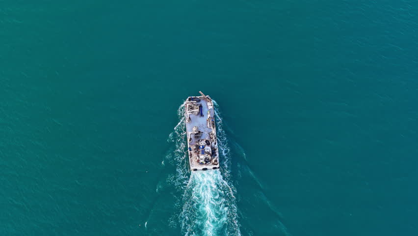 A boat makes its way across clear blue water under sunny skies. The surface reflects light as the vessel travels away from the shoreline.