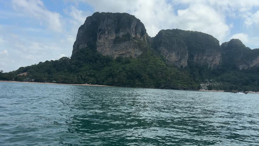 View from the ocean while approaching Railay Beach in Krabi, Thailand, showing calm sea water in the foreground and forested limestone cliffs rising along the tropical coastline