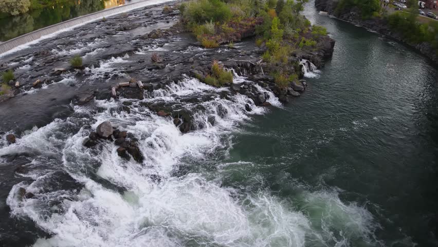 A small waterfall cascades over rocks into a clear river, creating white water rapids in a natural setting.