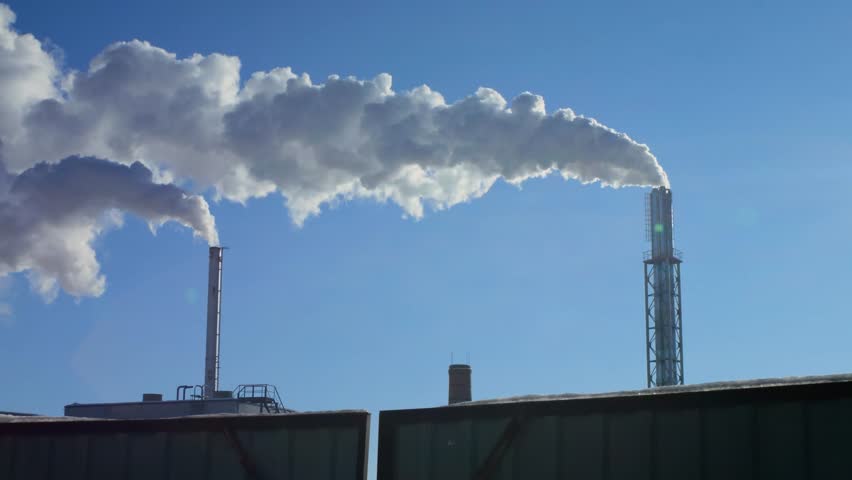 Smoke coming out of two tall factory chimneys against a blue sky. Steam coming out of two chimneys. Air pollution. Contrast.