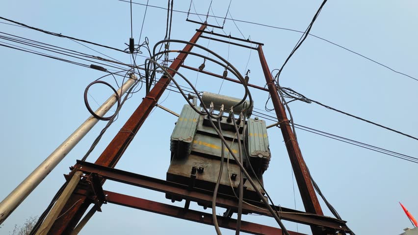 Camera orbiting around pole-mounted distribution transformer on H-type metal structure, showing connected cables, insulators and electrical hardware against clear sky background.