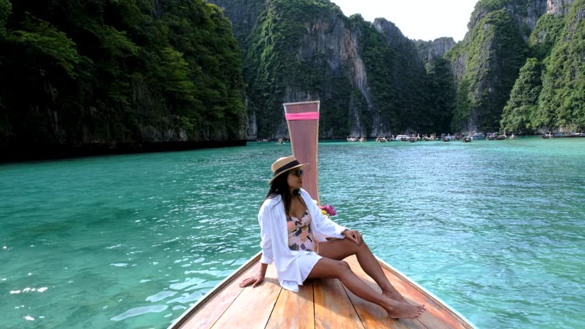 A woman relaxes on a traditional boat while soaking in the breathtaking beauty of Pileh Lagoon. Koh Phi Phi, Thailand