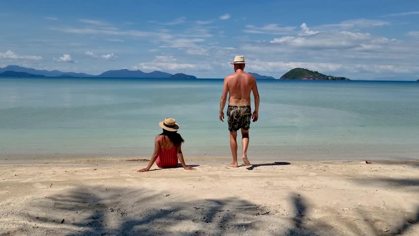 Two travelers enjoy a peaceful moment on the beautiful sandy beach of Koh Mak, Thailand. The calm water reflects the blue sky as they create unforgettable holiday memories.