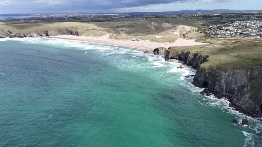 Aerial drone shot of the rugged coastline and sandy beach at Watergate Bay near Newquay, Cornwall, England, with turquoise sea and rolling waves.