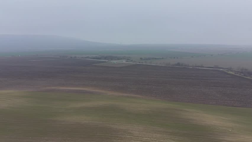 Aerial countryside landscape with long road across farming fields under overcast sky creating calm rural mood.