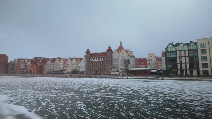 A scenic view of the historic Gdansk Old Town architecture along the frozen Motlawa River in Poland during a cold winter day.