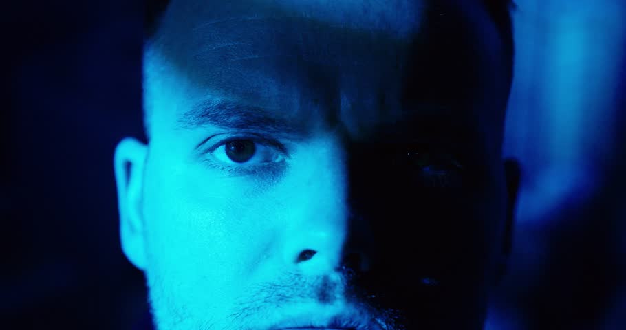Cinematic close-up of a man staring intensely into the camera under blue night lighting, conveying aggression, menace, tension, and a psychological thriller or stalker-like atmosphere.