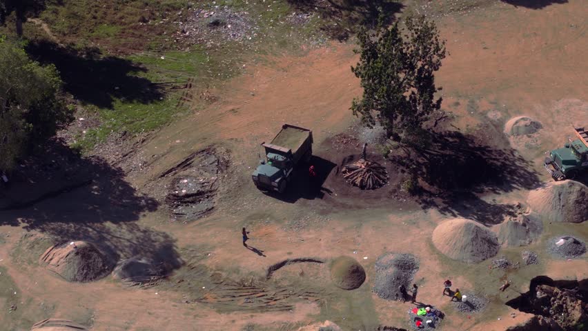 Manual laborers and trucks extracting sand and gravel from a riverbed for the construction industry in Haiti. Aerial drone orbiting