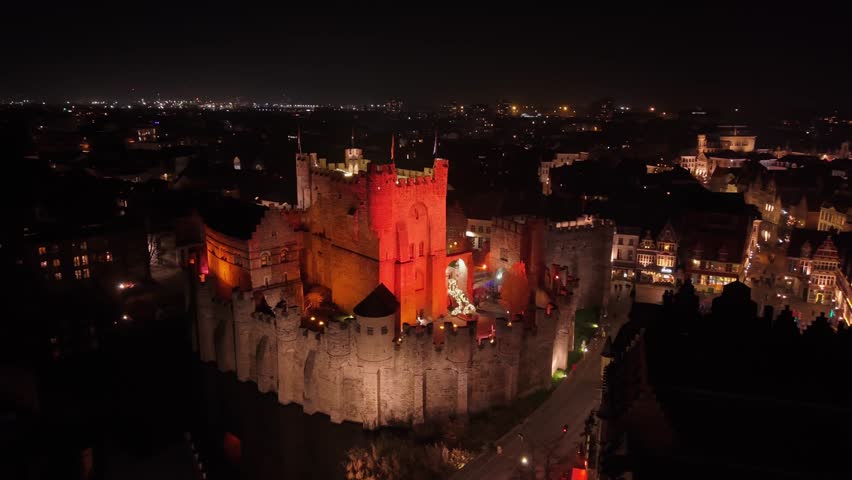 A 360-degree drone orbit around the medieval Gravensteen Castle in Ghent, Belgium, bathed in intense red light against the dark night sky.