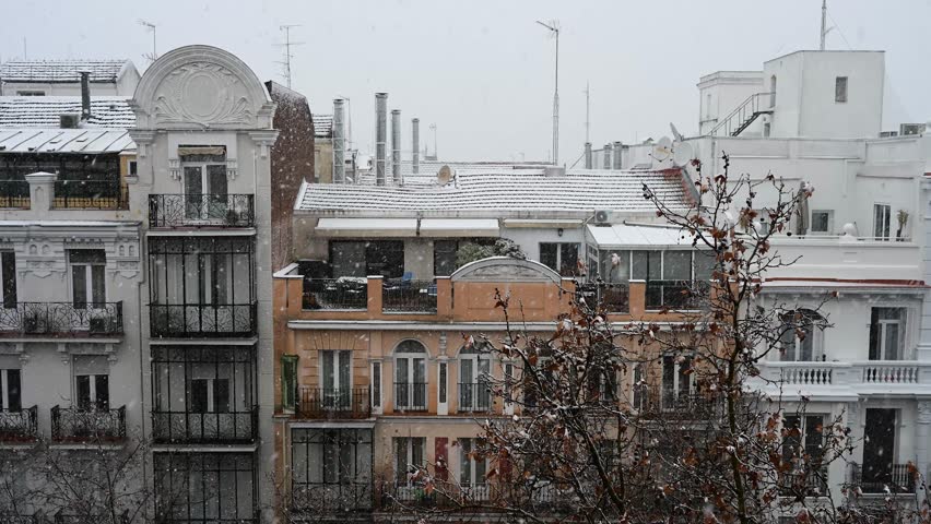 Madrid slow motion snow: Heavy winter storm covers historic architecture and balconies. White snowflakes fall on the city skyline and rooftops in Spain.