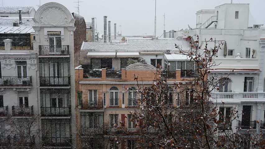 Snowstorm in Madrid: Slow motion view of heavy snow falling on residential buildings. Winter weather covers chimneys and autumn trees in the Spanish capital.
