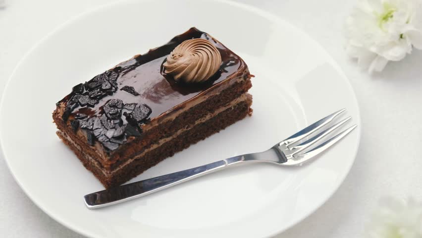 Decadent chocolate cake slice with frosting, served on a white plate with a fork.