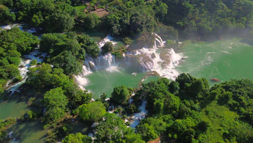 Stunning drone footage of Ban Gioc Detian Falls, showing multiple tiers of cascading water surrounded by lush tropical vegetation and turquoise pools in Cao Bang