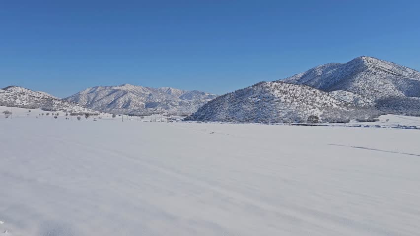 A wide snow-covered plain stretches toward rugged mountains under a clear blue sky on a bright, silent winter day.  
📍Marivan, Kurdistan 