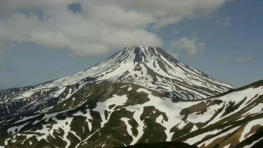 A majestic snow-capped mountain rises against a backdrop of clouds and blue sky, showcasing the beauty of nature in a serene landscape.