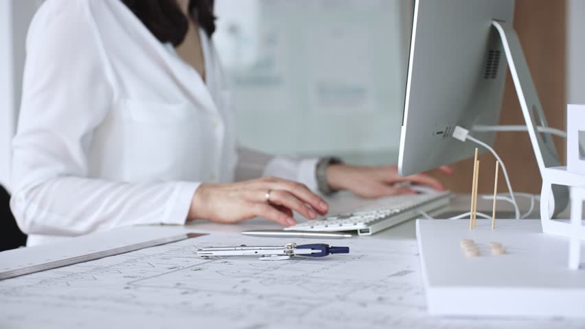 Architect creating new designs, working at a computer in office with blueprints and drafting tools. Business and architecture concept