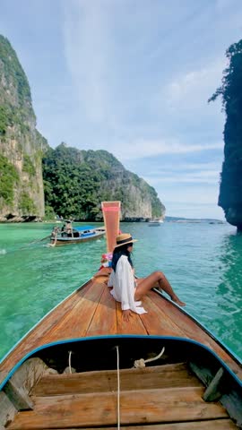 Enjoy a peaceful moment on a traditional boat in Koh Phi Phi, Thailand, surrounded by stunning cliffs and blue water. A perfect holiday vibe for relaxation and adventure seekers alike. Krabi, Thailand