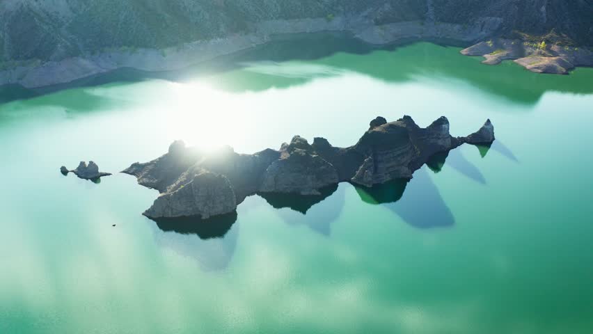 Angled aerial of dark rock islands surrounded by turquoise canyon water glistening sunlight, Canon Del Atuel, Mendoza Argentina