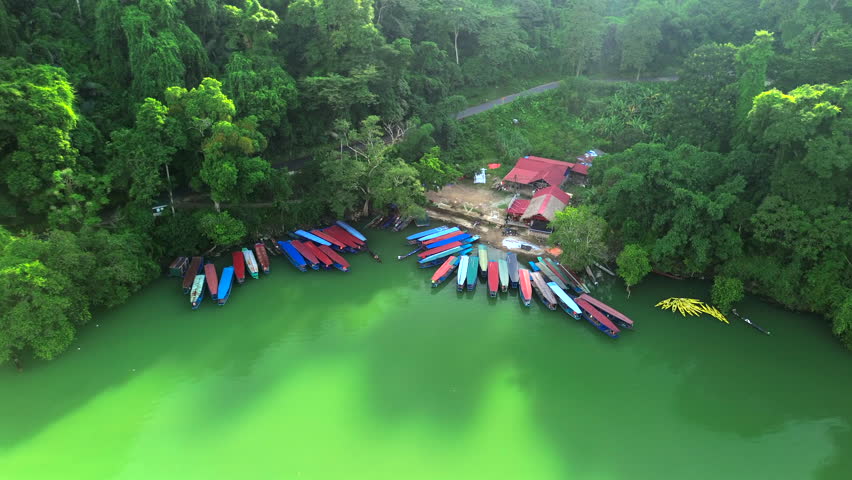 High-angle drone shot showing several traditional colorful boats parked on the turquoise waters of Ba Be Lake, surrounded by dense tropical rainforest and a small dock area.