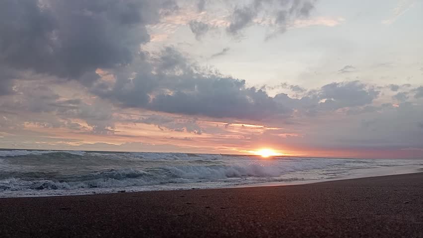 Cinematic sunset over the tropical ocean with waves crashing on the sandy beach.