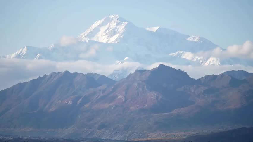 Aerial view of Denali rising above the clouds and surrounding peaks, showcasing North America’s tallest mountain in rugged Alaska wilderness.