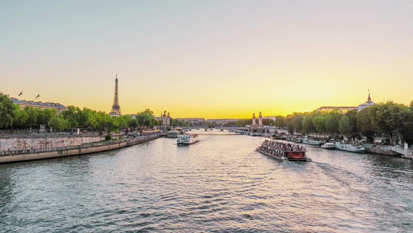 Time lapse of Paris sunset showcasing the Eiffel Tower and Pont Alexandre III with shimmering reflections on the Seine River, France. Romantic cityscape with historic architecture, glowing lights, and dramatic evening sky in a famous European travel destination.