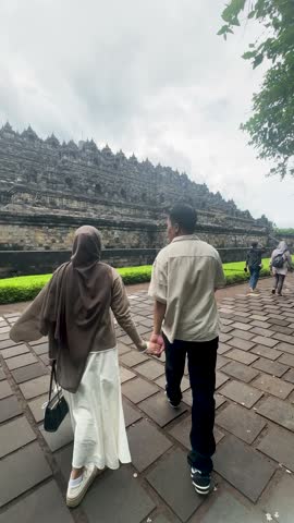 Indonesian couple vacationing at Borobudur Temple, amidst the green trees and ancient rocks