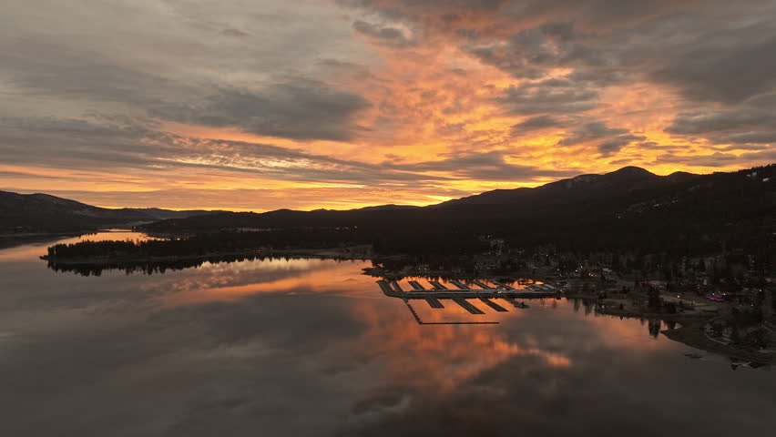 Golden sunrise over Big Bear Lake with glowing clouds mirrored on calm mountain waterscape