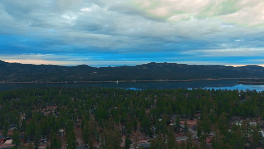 Wide view of Lake framed by forest and mountains under dramatic cloudy sky with layered horizon depth